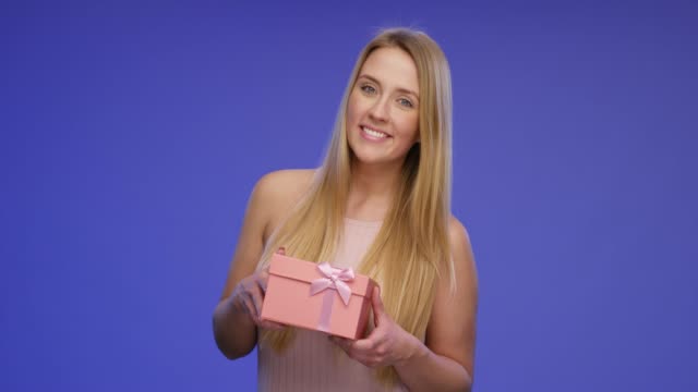 Wunderschöne-lächelnde-Frau-hält-eine-Geschenkbox-mit-der-Kamera
