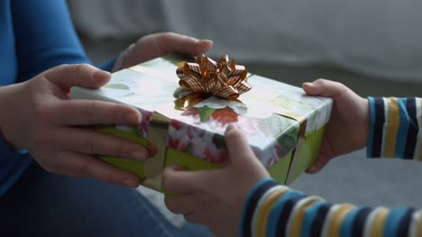 Child-hands-giving-holiday-gift-box-to-his-mother
