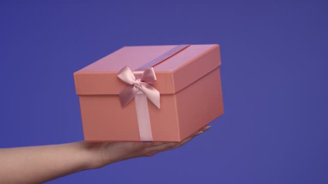 Mano-de-mujer-sosteniendo-una-hermosa-caja-de-regalo-en-pantalla-azul;-Concepto-de-celebración