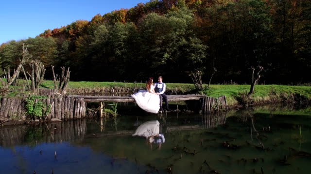 Die-Bräute-sitzen-in-der-Nähe-des-Sees-auf-einer-kleinen-Brücke-im-park