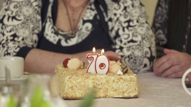 Ältere-Frau-Ausblasen-der-Kerzen-auf-der-Geburtstagstorte-am-Esstisch