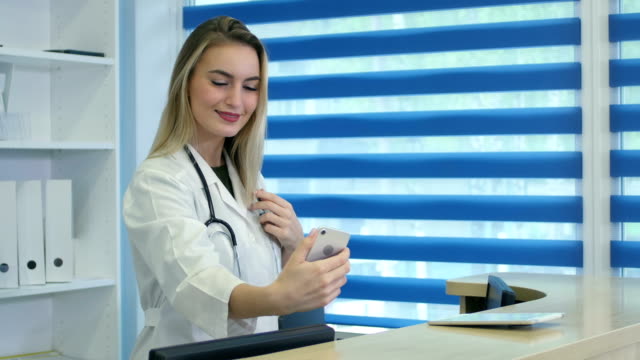 Enfermera-sonriente-tomar-autorretratos-con-su-teléfono-detrás-de-recepción