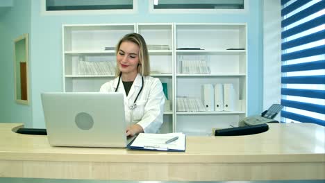 Smiling-medical-nurse-working-on-laptop-and-making-notes-at-reception-desk