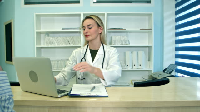 Smiling-nurse-with-laptop-scheduling-appointment-for-male-patient-at-reception