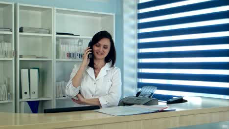 Smiling-female-nurse-answering-phone-call-at-the-reception-desk