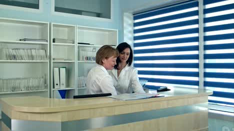 Smiling-female-doctors-standing-at-the-reception-desk-in-hospital