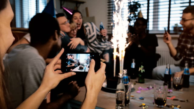 Weibliche-Hände-fotografieren-Smartphone-multiethnischen-Geburtstags-Party-mit-Feuerwerk-Kerzen,-Freunde-umarmen-Zeitlupe
