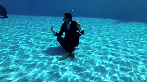 Ein-Mann-in-einem-Anzug-und-ein-weißes-Hemd-meditiert-unter-dem-Wasser-in-den-Pool-in-einem-Lotussitz.-Er-sitzt-auf-dem-Boden-und-schaut-sich-um.-Slow-Motion.-Action-Kamera-unter-Wasser.