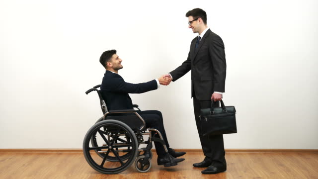 Der-Behinderte-und-ein-Geschäftsmann-Handshake-auf-dem-weißen-Wandhintergrund
