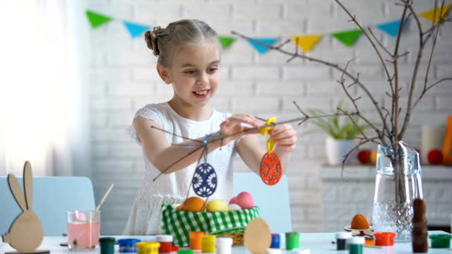 Kleines-Mädchen-hängen-von-Hand-gefertigte-Spielzeug-Eier-auf-Ästen,-Oster-Deko