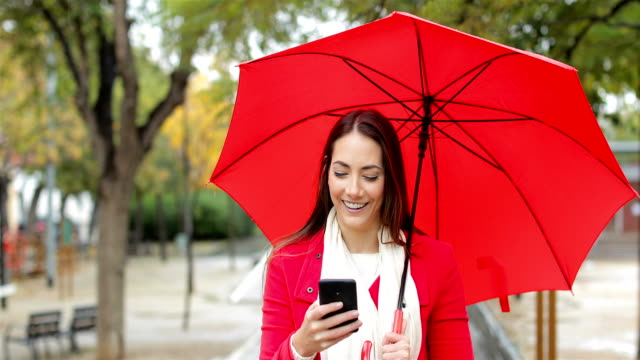 Mujer-feliz-en-rojo,-comprobación-de-teléfono-bajo-la-lluvia