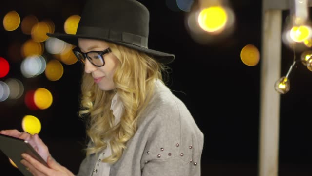 Blonde-Woman-Smiling-and-Using-Tablet-in-Night-City
