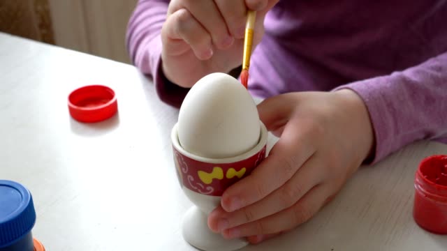 Primer-plano,-el-huevo-de-Pascua-blanco-se-levanta-sobre-un-soporte,-y-el-niño-lo-dibuja-con-un-pincel.-4k.