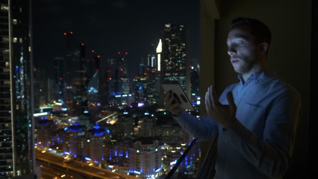 Hombre-joven-usando-la-tableta-para-hablar-y-comunicarse-con-el-fondo-de-la-vista-rascacielos