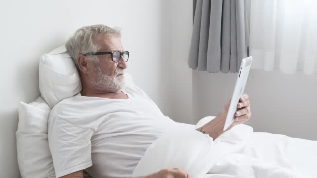 Großvater-oder-Seniorenmensch-mit-Tablet-Technik-und-aufmuntern-auf-dem-Bett