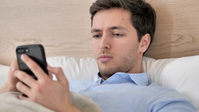 Junger-Mann-mit-Smartphone-in-Bett