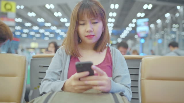 Slow-motion-Asiatische-Frau-mit-Smartphone,-während-sie-auf-dem-internationalen-Flughafen-sitzt.