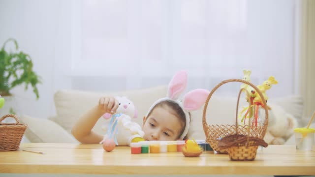 Little-cute-and-adorable-girl-is-smiling-and-playing-with-colorful-chicken's-eggs-and-bunnies.-Bunny-eats-its-favourite-food--Easter-egg.-Concept-Easter-holiday.