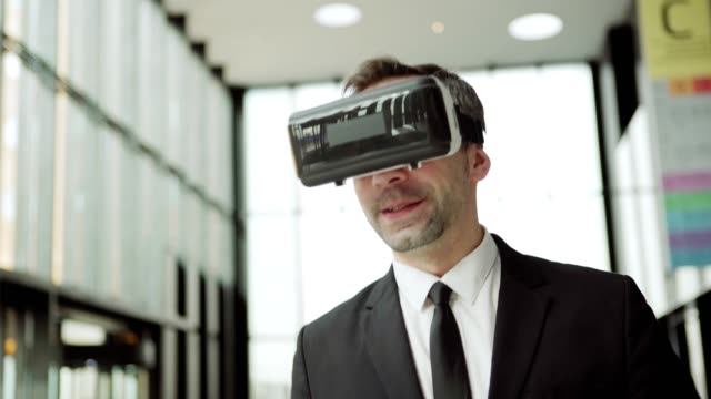 Medio-tirador-de-hombre-de-negocios-moderno-en-traje-formal-y-gafas-de-realidad-virtual-caminando-a-lo-largo-del-centro-de-negocios-y-participando-en-videoconferencia
