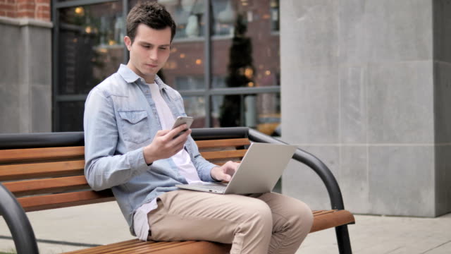 Junge-Mann-sitzt-auf-Bank,-während-er-online-arbeitet