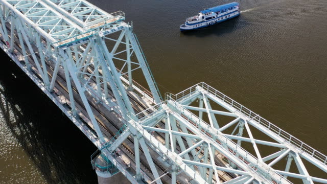 Aerial-view-of-the-railway-bridge,-with-a-moving-train-on-it,-across-the-river-flowing-through-a-major-city