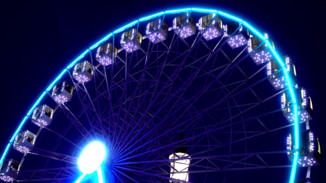 4K-view-of-illuminated-ferris-wheel-rotates-against-a-dark-sky.