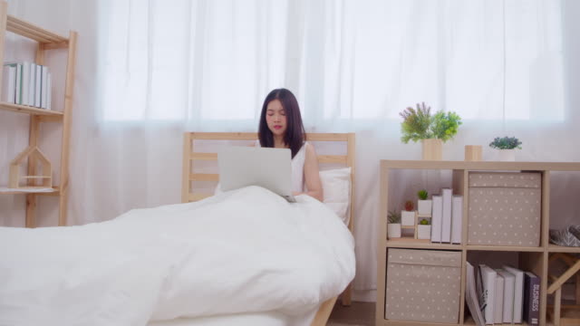 Joven-empresa-freelance-mujer-asiática-trabajando-en-portátil-revisando-las-redes-sociales-mientras-se-acuesta-en-la-cama-cuando-se-relaja-en-el-dormitorio-en-casa.-Concepto-de-mujer-de-estilo-de-vida-en-casa.