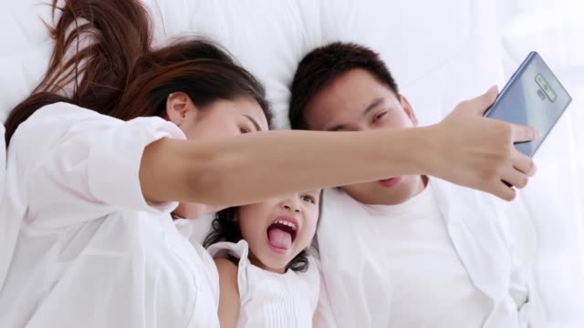 Familia-asiática-se-acuesta-sobre-en-la-cama-jugando-y-buscando-aplicación-teléfono-inteligente-mientras-está-acostado-en-el-dormitorio