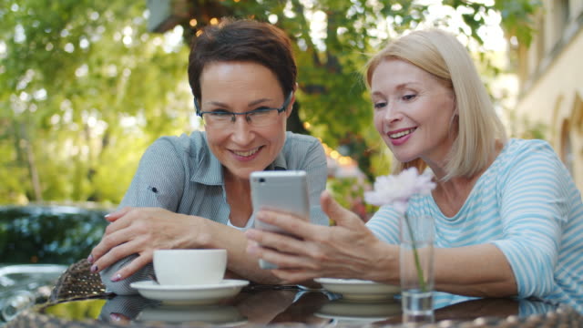 Cámara-lenta-de-mujeres-bonitas-usando-teléfono-inteligente-en-café-al-aire-libre-sonriendo