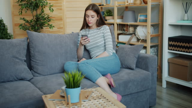 Slow-motion-of-young-lady-with-serious-face-using-smartphone-at-home-on-couch