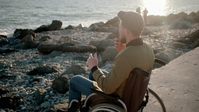 Behinderter-Mann-spricht-auf-dem-Handy-am-Ufer