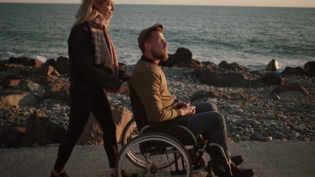 Mujer-cuidando-de-marido-discapacitado-y-caminando-con-él-por-el-mar