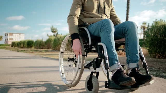 El-joven-usuario-masculino-de-la-silla-de-ruedas-está-rodando-sobre-las-calles-de-la-ciudad,-vista-detallada-de-las-piernas