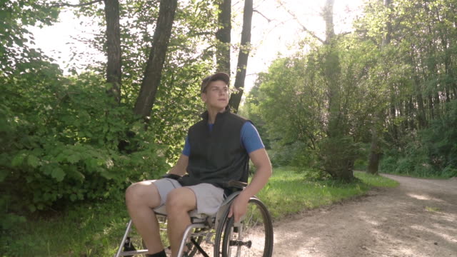 Slowmotion-front-face-follow-of-disabled-young-student-man-in-a-wheelchair-observing-nature-around-him,-with-sun-flare
