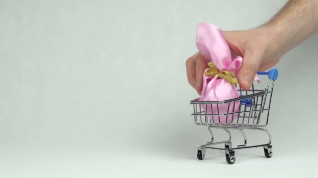 Mann-Hand-legt-ein-rosa-Geschenk-Osterei-in-einem-Einkaufskorb-weißen-Hintergrund,-Kopierplatz,-Konzept-Supermarkt