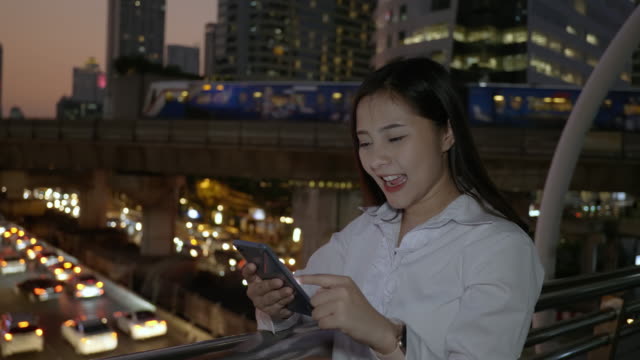 Excited-business-asian-woman-celebrating-good-news-checking-smart-phone-in-the-modern-city-center-in-the-night-of-Bangkok-Thailand.-Concept-Technology-communication,-success-by-mobile-phone