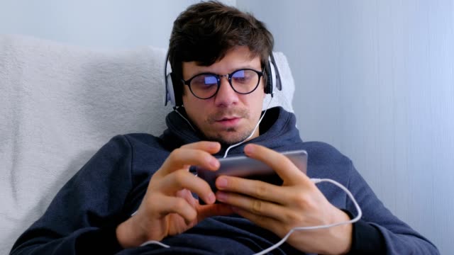 Mann-in-Brille-und-Kopfhörer-Online-Browsing-auf-dem-Smartphone.-Gesicht-Nahaufnahme.