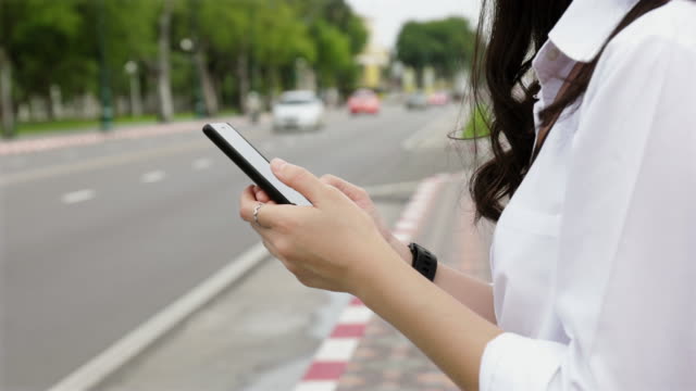 Close-up-hands-young-woman-typing-a-message-on-a-smartphone-while-standing-beside-the-street-in-Bangkok-Thailand.