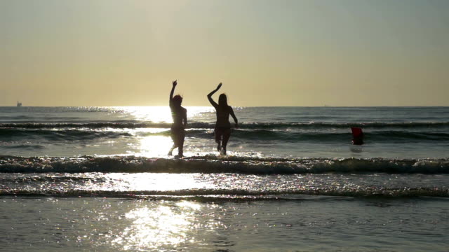 Silhouettes-of-two-beautiful-girl-friends-having-fun-and-playing-in-the-ocean-in-slow-motion