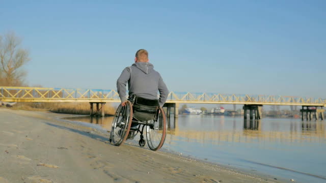 Disabled-person-in-a-wheelchair,-back-view,--goes-along-embankment-