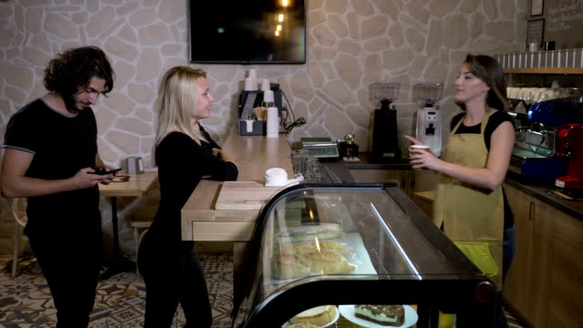 Junge-und-schöne-Kunden-in-einem-Café-Getränke-bestellen-und-bezahlen-mit-Kryptowährung-Bitcoin-mit-ihrem-smartphone