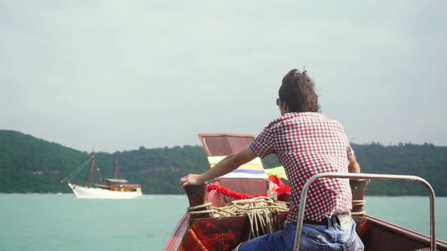 Young-traveler-man-enjoying-sailing-boat-on-sea-sits-on-nose-of-a-wooden-boat-and-looks-on-floatinf-ship,-slow-motion.-1920x1080
