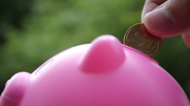 Hand-putting-coins-in-a-pink-piggy-bank,-saving-money-concept