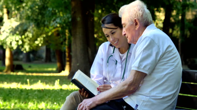 Una-niñera,-enfermera,-cuidar-a-los-ancianos-una-chica-(mujer)-y-el-abuelo-se-sientan-en-un-libro-y-leer-un-libro,-en-el-parque.