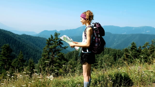 Woman-tourist-with-a-backpack-stands-against-a-beautiful-landscape-and-holds-a-paper-map-and-looks-into-the-distance.-Girl-looking-for-a-route