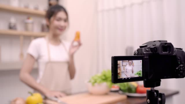 Blogger-Asian-woman-using-camera-recording-how-to-make-salad-healthy-food-video-for-her-subscriber,-female-use-organic-vegetables-preparing-salad-for-fit-body-at-home.-Healthy-food-concept.