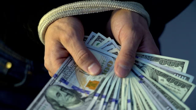 male-hand-bound-with-the-rope-holding-pile-of-money-american-dollar-bank-notes,-financial-rectrictions-concept