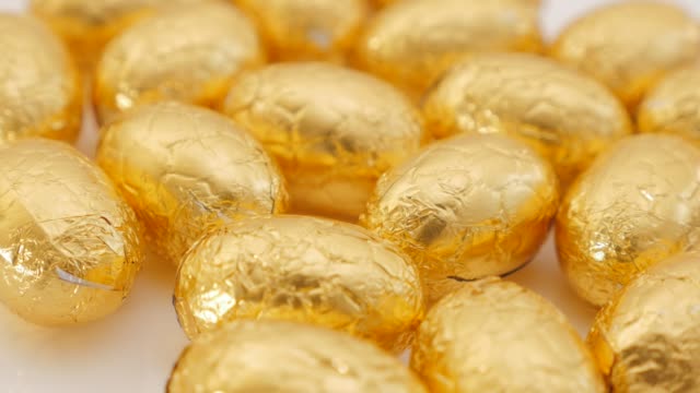 Lot-of-golden-foil-wrapped--Easter-chocolate-eggs-on-white-background--4K-3840X2160-30fps-UHD-footage---Traditional-Easter-gold-eggs-on-white-surface-4K-2160p-UltraHD-video