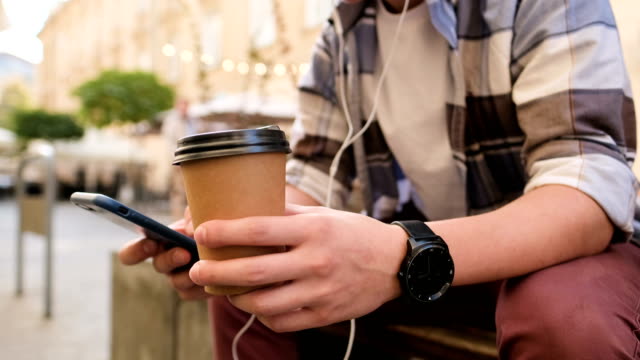 Mann-nutzt-Smartphone-und-trinkt-Kaffee,-um-ins-Freie-zu-gehen.-Close-up.-Generation-z-oder-Blogger,-mit-seinem-Smartphone,-scrollt-durch-Social-Media-Feed-auf-dem-Gerät,-Überprüfung-Karte,-lesen-Nachrichten-auf-App