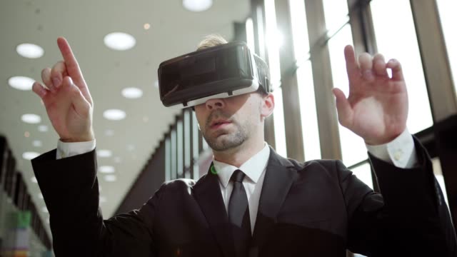 Panning-medium-shot-of-modern-middle-aged-businessman-in-VR-headset,-exploring-analytical-data-visualized-in-virtual-reality-standing-in-sunlight